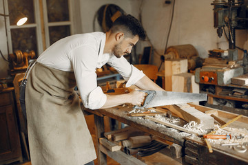 Man working with a wood. Carpenter in a white shirt. Worker with a saw