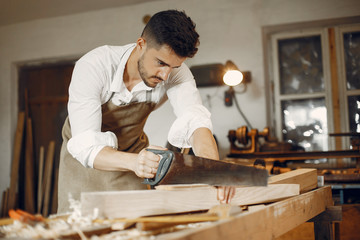 Man working with a wood. Carpenter in a white shirt. Worker with a saw