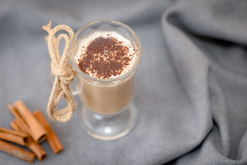 Traditional winter eggnog in glass mug with milk, cinnamon and chocolate covered with whipped cream on a gray cloth,cinnamon sticks on cloth background. Advertising for cafe menu. Coffee.