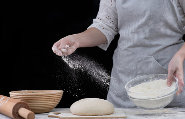 Baker sprinkles flour on a dough for cooking pastries, bread or pizza. Isolated on dark background