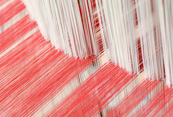 Close up of interlacing between white warp yarn and red weft yarn on traditional cotton weaving loom. Selective focus.