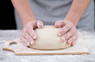 Fototapeta premium Female hands hold the dough. baker forms homemade bread