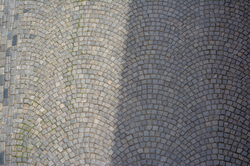 The road is paved with setts divided in half by a dense shadow