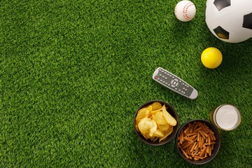 Soccer ball on a green field and ottoman for a fan with snacks and a TV remote control. flat lay.Copy space.