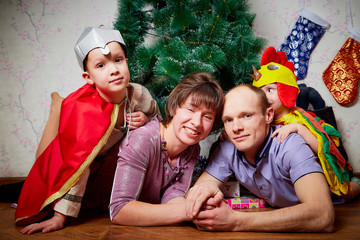 Family consisgitng mother, father and two brothers in carnival costumes at Christmas or new year near the Christmas tree in the room. Mom, dad and boys indoor
