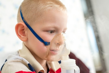 Sick boy inhaling through inhaler mask, face close-up view. Use nebulizer and inhaler for the treatment