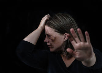 Crying woman victim of domestic violence and abuse showing a stop sign and closes her mouth with her hand. Isolated on dark background