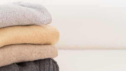 Stack of cozy knitted sweaters in beige grey colour on white background with copy space.  Warm...