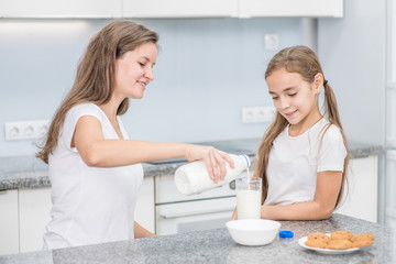 Fototapeta premium Smiling young woman and her little cute daughter have breakfast at home