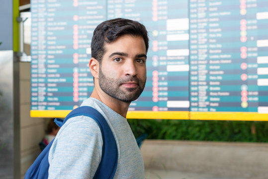 Serious Hispanic man posing near departure board. Focused bearded guy looking at camera. Travel concept