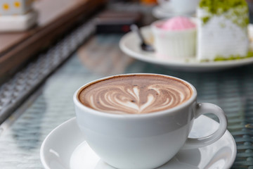 Hot latte art coffee heart shape in a white cup on wooden table with blurred background, selective focus