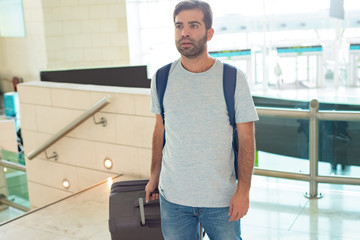 Medium shot of focused young man with luggage. Handsome Hispanic traveler looking at distance at airport. Travel concept