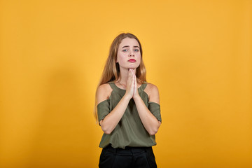 Portrait of worried young woman in vivid casual clothes looking directly, holding hands crossed, praying isolated on bright orange wall background in studio. People lifestyle concept.