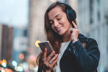 Young happy stylish trendy casual hipster woman changes songs and tracks on smartphone during...