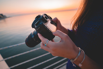 Woman photographer holds dslr camera during taking photos sea at sunset