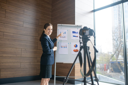 Dark-haired woman smiling while filming business blog for her followers