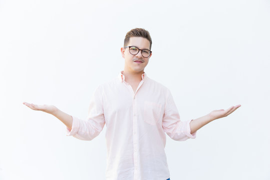 Skeptical guy in eyeglasses shrugging or pointing hands at both sides. Young man in glasses standing isolated over white background. Advertising concept