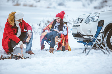 man with woman sitting on chairs near camp fire in winter time. car travel. - Powered by Adobe