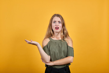 Pretty young caucasian woman over isolated orange wall keeping hand up, looking directly, showing space for advertising wearing funny clothes