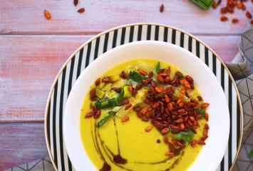 Spring leek cream soup with potatoes and roasted paprika seasoned sunflower seeds in white bowl on striped plate.