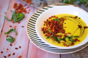 Spring leek cream soup with potatoes and roasted paprika seasoned sunflower seeds in white bowl on striped plate.