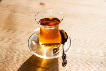 Turkish tea in a glass with sugar cubes and a spoon on a wooden table