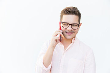 Pensive smiling guy in eyeglasses calling cell and looking away. Young man in glasses standing isolated over white background. Mobile phone talk concept