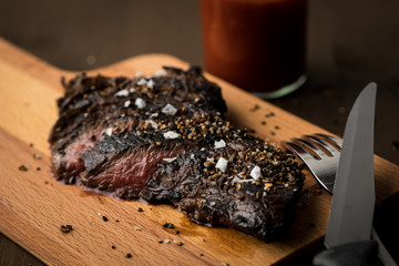 Rinder Hüftsteak auf Holzbrett mit Ketchup, Salz und Steakpfeffer auf Holz Hintergrund dunkel