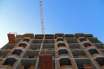 The facade of red brick modern residential building under construction. Building construction site with crane above the blue sky background. The construction of modern apartment buildings