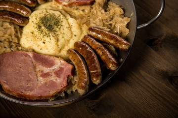 Sauerkraut Pfanne mit Nürnberger Rostbratwürste, Kassler Nacken und Kartoffelpüree auf Holz Tisch