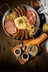 Sauerkraut Pfanne mit Nürnberger Rostbratwürste, Kassler Nacken,  Kartoffelpüree, Senf und Gewürze Zutaten auf Holz Tisch