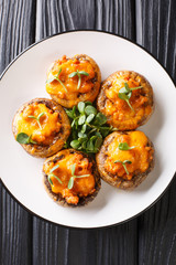 Baked Portobello mushrooms with minced meat and cheddar cheese close-up on a plate. Vertical top view