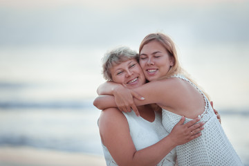 Portrait of a happy mother and adult daughter. They hug on the background of the sea.