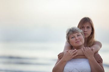 Portrait of a happy mother and adult daughter. They hug on the background of the sea.