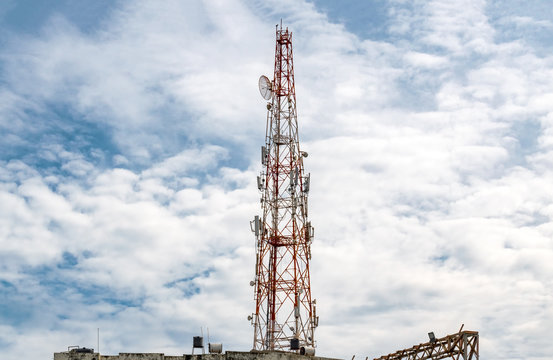 Tall Mobile Phone Tower, Celluar Tower with umbrella dish, attenuators, amplifiers and repeaters, installed on rooftop and is rising high in the Sky with Dramatic Sky background on a sunny noon. -