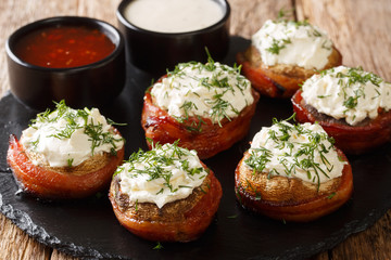Cheese stuffed mushrooms wrapped in bacon served with sauces close-up on a plate. horizontal