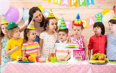 Group of adorable kids, birthday girl and her mom gathered around festive table. Birthday party for preschoolers