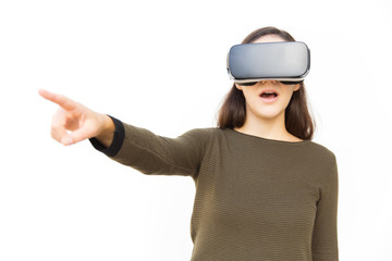 Shocked excited student in VR headset pointing finger away. Young woman in casual and virtual reality glasses standing isolated over white background. Advertising concept