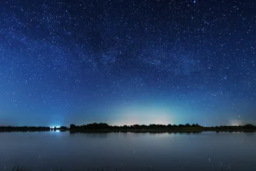 Fototapete Sternenhimmel A magical starry night on the river bank with a large tree and a milky way in the sky and falling stars in the summer.  © reme80