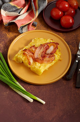Cheesy potato bake with fried bacon, pickled tomatoes and green onion on yellow plate
