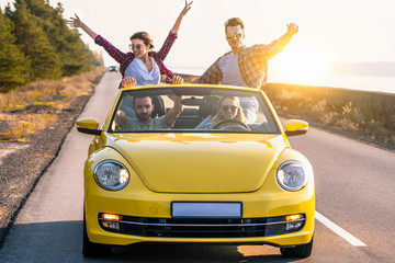 The happy friends are traveling by a yellow cabriolet