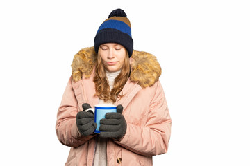 young woman in winter clothes warms her hands on a hot mug