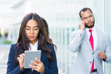 Obraz premium Closeup shot of focused Asian worker using tablet. Concentrated young businesswoman holding tablet on street. Technology concept
