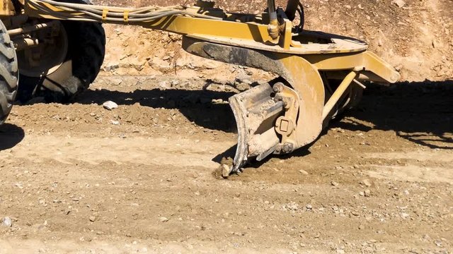 Close-up of moldboard planning road surface. Blade of motor grader during road construction works. Earthmoving, excavations, digging on the rocky soils.