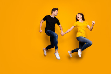 Fototapeta na wymiar Full size photo of funny guy and lady couple jumping high rushing mall black friday final discounts season wear casual jeans black t-shirts isolated yellow color background