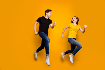 Fototapeta na wymiar Full size photo of sporty guy and lady couple jumping high active way of life pair marathon participants wear casual jeans black t-shirts isolated yellow color background