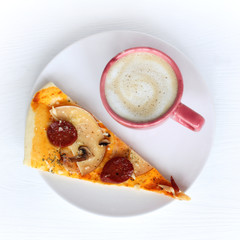 mug with coffee and a slice of pizza with salami and smoked cheese, mushrooms, seasoning top view. hot quick breakfast