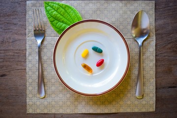 Vitamin pills served with spoon and fork in plate on the wooden table