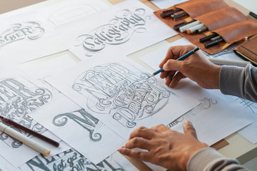 Typography Calligraphy artist designer drawing sketch writes letting spelled pen brush ink paper table artwork.Workplace design studio. - Powered by Adobe