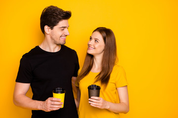 Photo of cheerful positive fun cute nice pretty couple of two spouses hugging while drinking hot beverage isolated in black t-shirt over yellow vibrant shiny color background